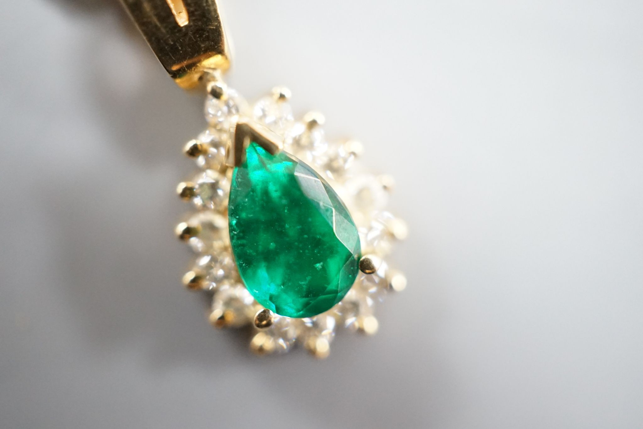 A modern 18k, emerald and diamond cluster set pear shaped pendant, overall 21mm, on an 18k chain, 43cm
